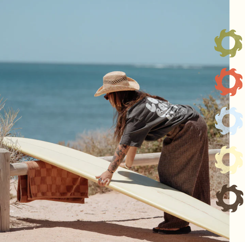 Person holding a surfboard by the ocean wearing onshore co. longboards and lassos boxy tee with decorative elements on a white background